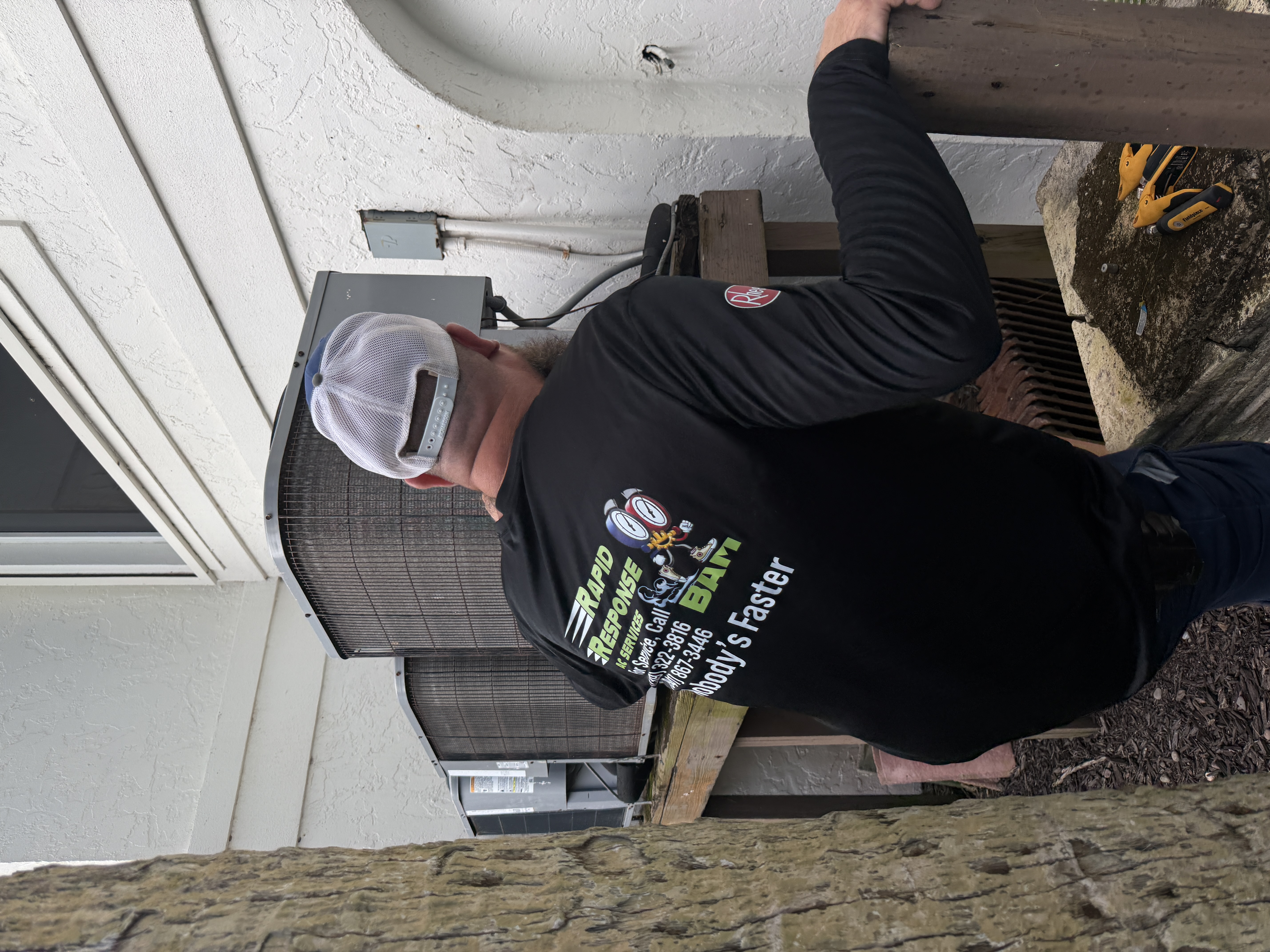 Rapid Response AC tech reaching toward outdoor condenser unit at a Southwest Florida home