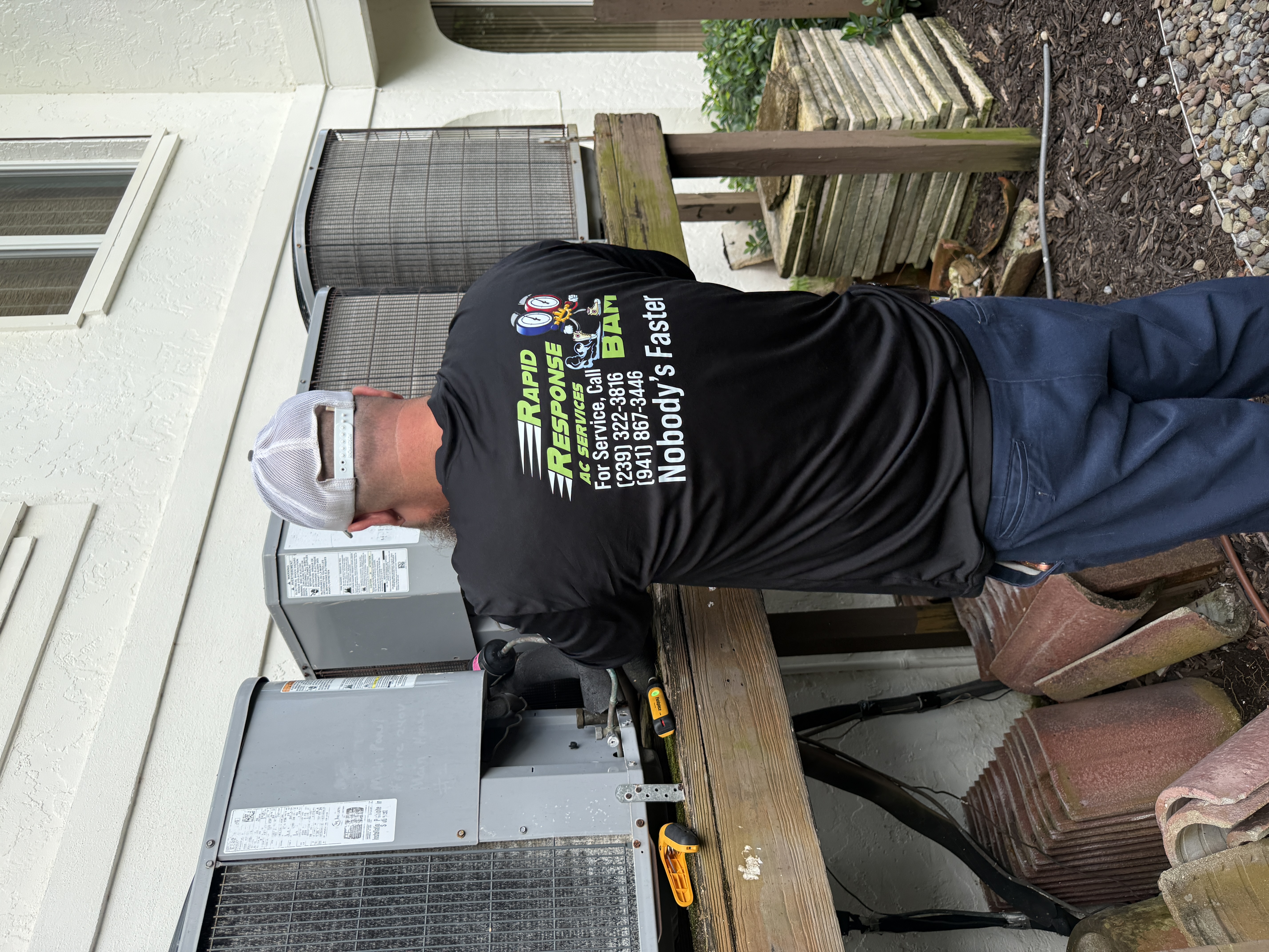 Rapid Response technician from behind working at two outdoor AC condensers on a residential property